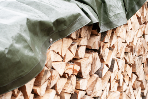 Bois de chauffage fendu couvert avec une bâche verte, stockage extérieur